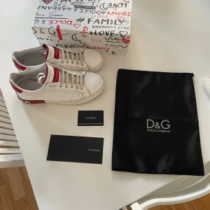 Vita sneakers från Dolce & Gabbana med röda detaljer - Säljer ett par riktigt feta dolce Gabbana skor i storleken 44 i fint skick såklart äkta finns äkthets bevis som syns på bilderna finns det fler frågor är det bara att skriva 🤗🙌