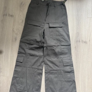 Grå cargobyxor opium swag  - Säljer ett par grå cargobyxor med flera stora fickor på benen och klassisk cargostil. Byxorna har dragkedja och knapp i midjan samt hällor för bälte. Perfekta för en streetwear-look. Storlek 28/XS. Något fel med knappen, den är lös, kan fixas såklart 