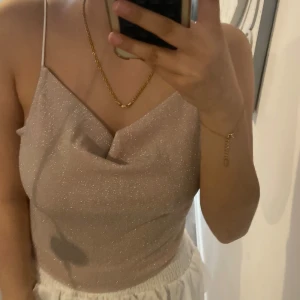 Glittrig beige linnetopp med tunna axelband - Säljer en glittrig beige linnetopp med tunna vita axelband och snygg drapering framtill. Perfekt för dig som vill ha en stilren men ändå festlig topp till sommaren.