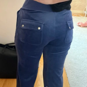 Mörkblå velourbyxor från Juicy Couture - Mörkblå mjukisbyxor från Juicy Couture i glansig velour med bred resår i midjan och snörning. Byxorna har raka ben och två fickor med knappar bak. Super bra skick, använd endast en gång❤️❤️