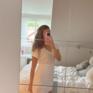 Vit tight kortklänning med rynkade detaljer - Säljer en vit tight kortklänning med korta ärmar och rynkade detaljer längs sidorna. Klänningen har en enkel och stilren design med rund halsringning och figurnära passform. Perfekt för dig som gillar en clean look.