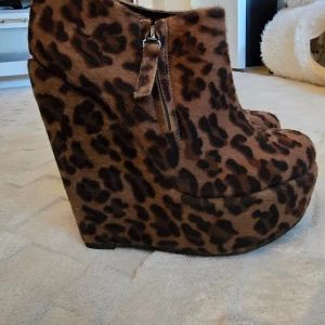 Leopardmönstrade klackar med dragkedja - Säljer ett par snygga kilklackar med leopardmönster och dragkedja på sidan. Skorna har hög platå och är täckta i ett mjukt syntetmaterial. Perfekta för dig som vill sticka ut med ett djurmönster och få extra höjd.