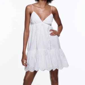 Vit somrig klänning med broderade detaljer - Säljer en superfin vit klänning med tunna axelband och v-ringning. Klänningen har broderade håldetaljer och volang nertill, perfekt för varma dagar. Lätt och luftig modell som ger en avslappnad känsla.