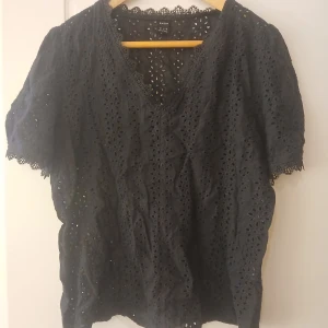 Svart spetsblus från SHEIN - Säljer en svart blus från SHEIN med v-ringning och korta ärmar. Blusen är täckt av broderade spetsdetaljer och har ett luftigt, elegant mönster. Perfekt att styla till olika outfits!