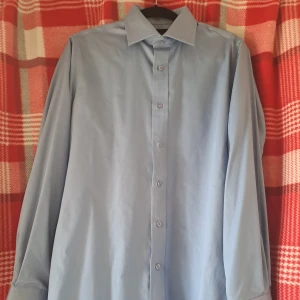 Ljusblå skjorta från Batistini - Snygg ljusblå skjorta från Batistini i 100% egyptisk bomull. Klassisk modell med lång ärm och knappar framtill. Perfekt för dig som vill ha en stilren och bekväm skjorta till vardags eller mer uppklädda tillfällen.