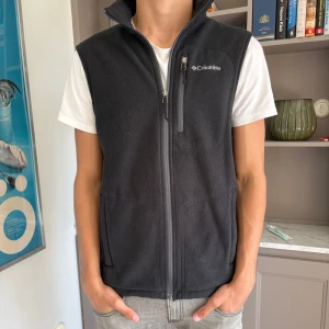 Columbia fleeceväst - Säljer en riktigt snygg svart fleeceväst från Columbia i mycket bra skick. Västen har en dragkedja framtill och en praktisk bröstficka. Perfekt för lager på lager under höst och vår eller för goa sommarkvällar. Killen på bilden är 178 cm och väger 66 kg.