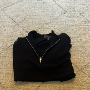 Svart långärmad tröja med dragkedja från H&M - Svart långärmad tröja från H&M i slim fit-modell. Tröjan har en kort dragkedja vid halsen och är tillverkad i ett mjukt material. Perfekt för en stilren och enkel look.