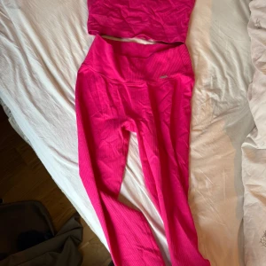 Rosa ribbade träningstights och top - Säljer ett par starkt rosa ribbade träningstights med hög midja och en matchande topp. Tightsen har en tight passform och är gjorda i ett stretchigt syntetmaterial som passar perfekt till gymmet eller yoga.