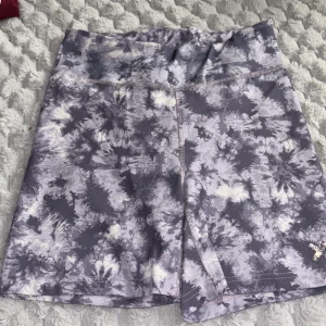 Grå-vita träningsshorts med batikmönster - Snygga träningsshorts i grått och vitt batikmönster från 15%. De har en hög midja och är tillverkade i ett stretchigt syntetmaterial som passar perfekt för träning. Modellen är tight och bekväm med sömmar som ger extra stöd.