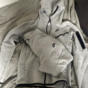 Nike Tech Set St.XS - Säljer ett ljusgrå Nike Tech set i mycket bra skick i st.XS. Setet har andvänts fåtal gånger och köptes för Hoodie:1200kr och mjukisbyxor:700kr. De är riktigt sköna med en snygg look!