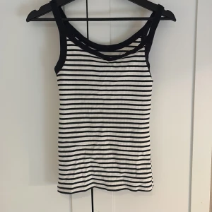 Randig ribbad linnetopp från H&M - Säljer en mörkblå-vit ribbad linnetopp från H&M med smala axelband och klassiskt randigt mönster. Toppen har mörkblå kanter och är perfekt för varma dagar. Superenkel att matcha med jeans eller kjol!