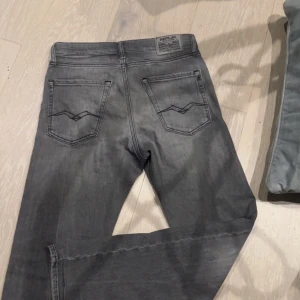 Grå jeansbyxor från Replay - Säljer ett par grå jeansbyxor från Replay med klassisk femficksdesign och raka ben. Byxorna har diskreta slitningar och en snygg tvättad look. Perfekta för dig som gillar en stilren och enkel vardagsstil.