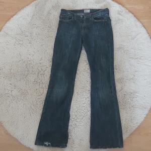 Vintage mörk blå bootcut jeans  - Mörkblå jeans från Tommy Hilfiger med bootcut-passform och klassisk femficksdesign. Jeansen har låg midja/mid rise, dragkedja och knapp framtill. Finns ett pytte litet hål på botten som visas på bild. 