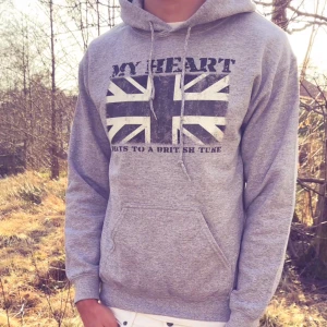 Grå hoodie från Drakenberg - Grå hoodie med tryck av brittiska flaggan och texten 'MY HEART BEATS TO A BRITISH TUNE' på bröstet. Klassisk huva med dragsko och magficka. Perfekt för en avslappnad stil.