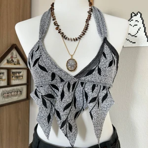 Assymetrisk halterneck topp - Unik svartvit linnetopp med halterneck och knyt i nacken. Toppen har ett coolt bladliknande mönster och spetsiga kanter nedtill som ger en edgy look. Perfekt för dig som vill sticka ut med en kreativ och trendig stil. 