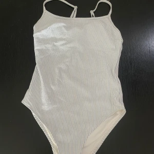 Randig baddräkt med smala axelband - Snygg baddräkt med smala axelband. Inlägg i brösten. Mönstret är randigt i vitt och ljusblått. Använd några få gånger.