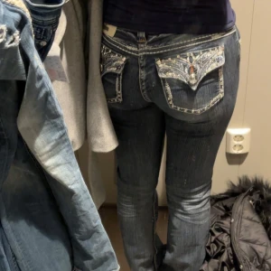 Mörkblå jeans med blingade fickor - Säljer ett par mörkblå jeans med låg midja och detaljer på bakfickorna, som är dekorerade med bling och stenar . Jeansen är bootcut och sitter bra på mig som är 168 cm. Jeansen är köpta i vintras för 1200kr och har använts av mig ca 5-7 gånger. Väldigt fint skick!