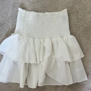 Vit volangkjol med smock - Supersöt vit kortkjol med bred smock i midjan och dubbla volanger. Kjolen har en luftig och flowy känsla, perfekt för varma dagar!!<3