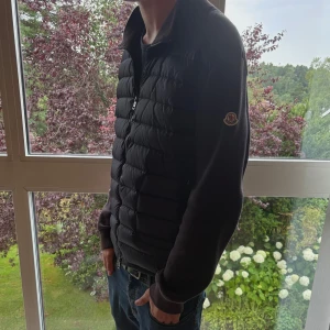 Moncler cardigan - Säljer en marin blå dunväst från Moncler med quiltad framsida och mjuka stickade ärmar. Västen har dragkedja framtill och klassisk Moncler-logga på ärmen. Perfekt för lager-på-lager och snygg till jeans eller hoodies. Den är sol blekt och där av priset. Hör av dig om frågor🔥🔥🔥