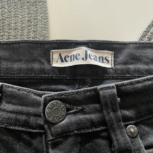 Svarta jeans från Acne Jeans - Snygga svarta jeans från Acne Jeans med klassisk femficksdesign och diskreta nitar. Jeansen har raka ben och normal passform, tillverkade i mjukt denimtyg. Perfekta för dig som gillar stilrena och tidlösa plagg. Kom med bud