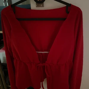 Röd omlottopp med knyt - Snygg röd omlottopp med djup v-ringning och knyt i midjan. Långärmad modell i mjukt tyg som ger en skön känsla. Perfekt för dig som vill ha en enkel men ändå trendig look.
