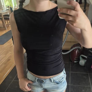 Svart ärmlös croppad topp - Säljer en svart, tight och croppad topp med ärmlös design och lätt rynkade sidor. Toppen har en enkel, stilren look med rund halsringning och passar perfekt till jeans eller kjol. Materialet känns mjukt och stretchigt, vilket gör den bekväm att bära hela dagen. (Slutsåld på gina tricot för tillfället.)