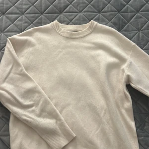 Beige stickad tröja från Zara - En stilren beige stickad tröja från Zara i storlek S. Tröjan har rund halsringning med ribbade detaljer och långa ärmar. Perfekt för lager-på-lager och enkel att matcha med jeans eller kjol.