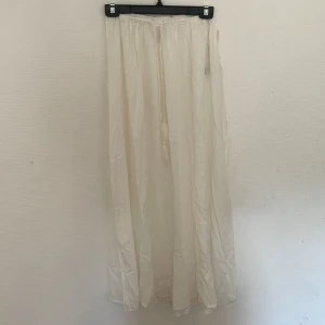 Vit långkjol från Nelly med snörning - Drömmig vit långkjol från Nelly i flowigt material. Kjolen har resår i midjan och snörning framtill för en skön och justerbar passform. Perfekt för en somrig och chill look. Aldrig använt