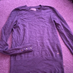 Grå långärmad tröja med knappar - Snygg grå långärmad tröja från Morris & White. Tröjan har ribbade muddar och dekorativa knappar vid ärmslutet. Perfekt för dig som gillar en enkel men stilren look. Materialet känns mjukt och lätt mot huden.