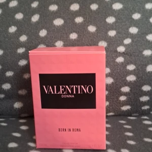Valentino Donna Born In Roma parfym - Exklusiv parfym från Valentino, Donna Born In Roma. Flaskan är i rosa glas med nitar och svart kork, och kommer i en snygg rosa kartong. Doften är feminin och modern, perfekt för dig som gillar lyxiga och trendiga parfymer.