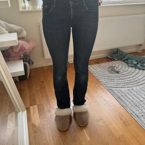Mörkblå bootcut jeans med låg midja - Snygga mörkblå bootcut jeans. Jeansen har låg midja, fem fickor och subtila kontrastsömmar. Perfekta för dig som gillar en tidlös look med lite extra edge. Materialet är stretchigt jeans för skön passform. Dock så har de lite slitning mellan benen.