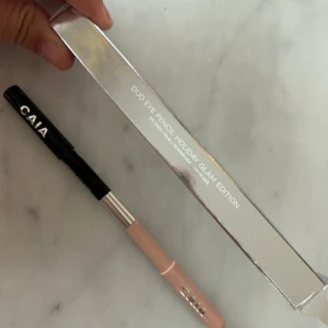 CAIA Duo Eye Pencil Holiday Glam - Duo ögonpenna från CAIA i Holiday Glam Edition. Ena sidan är en svart eyeliner och andra sidan en nude eye brightener. Pennan har stilren design med svart och beige färg samt silverdetalj i mitten. Perfekt för att skapa både markerade och ljusare ögonlooker.