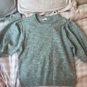 Grå stickad tröja från Gina Tricot - Supermysig grå stickad tröja från Gina Tricot med puffiga ärmar och ribbade muddar. Perfekt för lager på lager och chill dagar. Rund halsringning och loose fit gör den både snygg och bekväm.