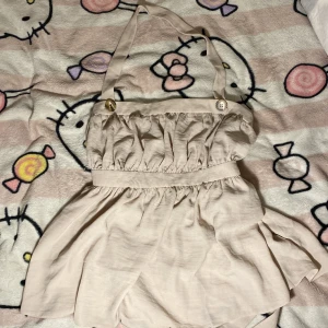 Beige topp från ASOS - Supersöt beige toop från ASOS med halterneck och knappar framtill. Toppen har volangig, rynkad överdel och markerad midja. Tillverkad i ett mjukt, lätt tyg som känns perfekt för varma dagar.