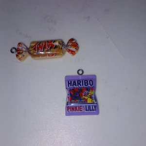 Söta godisberlocker Twix & Haribo - Två unika berlocker formade som godis: en Twix-karamell i gult och rött samt en lila Haribo Pinkie & Lilly-påse. Perfekta som halsbands- eller armbandsberlocker för dig som älskar färgglada och lekfulla accessoarer.
