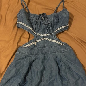 Blå jeans jumpsuit med cut-outs från Bebe - Supersnygg blå kort jeans jumpsuit från Bebe med cut-outs i midjan och vita detaljer.  har snörning upptill, dragkedja i sidan och ärmlös . Perfekt för dig som vill sticka ut med en cool och trendig look! Den har fickor väldigt fin och somrig 