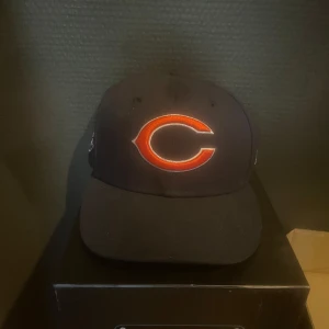 Chicago Bears keps New Era 59FIFTY - Snygg svart Chicago Bears keps från New Era 59FIFTY med broderad orange logga framtill och Super Bowl-märke på sidan. Klassisk rak skärm och NFL-märke på insidan. Perfekt för dig som gillar amerikansk fotboll och streetwear.