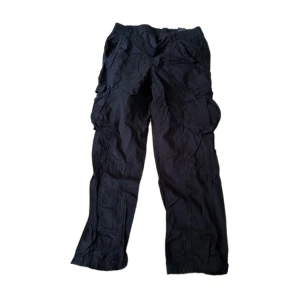 Svarta cargobyxor från Divided H&M, storlek 40 - Svarta cargobyxor från Divided H&M med elastisk midja och flera stora fickor på sidorna. Storlek 40. 