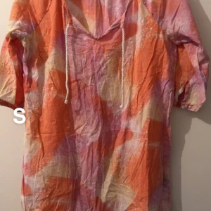 Färgglad tröja med snörning - Säljer en tröja i orange, rosa och vit med abstrakt mönster. Tröja har v-ringning med snörning och halvkort ärm. Perfekt för varma dagar och ger en riktigt somrig vibe.🌸Fint använt skick. Tunt material. Storlek s 