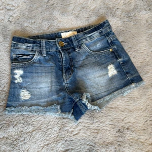 Blå jeansshorts med slitningar - Snygga blå jeansshorts från U med slitna detaljer och fransig kant nertill. Klassisk femficksmodell med knapp och dragkedja framtill. 