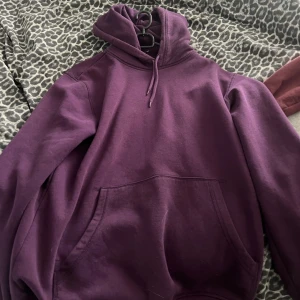 Lila hoodie med huva och ficka - En stilren lila hoodie med huva och snörning, samt en stor magficka framtill. Perfekt för dig som gillar en avslappnad och bekväm look. Tröjan har långa ärmar och är gjord i mjuk bomullsmix.
