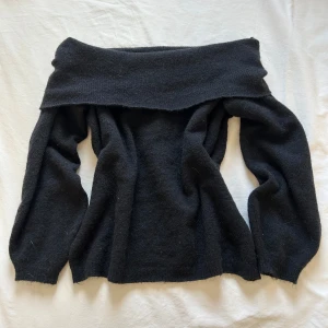 Svart offshoulder stickad tröja - Svart stickad tröja med offshoulder-design och långa ärmar. Mjuk och skön, perfekt för dig som gillar en stilren look med en twist. Passar till både jeans och kjol för en trendig vibe.