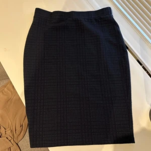 Mörkblå rutig pennkjol - Snygg mörkblå pennkjol med diskret rutigt mönster. Kjolen har en klassisk, figurnära passform och är knälång. 