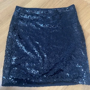 Svart paljettkjol från H&M Divided - Glittrig svart kortkjol från H&M Divided, täckt med paljetter för en riktigt festlig look. Kjolen är rak i modellen och tillverkad i polyester. Perfekt för dig som vill sticka ut med extra bling.