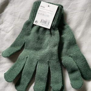 Gröna stickade handskar - Säljer ett par gröna stickade handskar med ribbad mudd. Perfekta för kalla dagar och enkla att matcha med din vinterjacka. Handskarna är mjuka och flexibla, vilket gör dem bekväma att bära hela dagen.