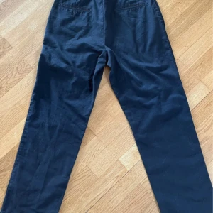 Svarta chinos med rak passform - Snygga svarta chinos med klassisk rak passform och diskreta fickor bak. Byxorna har bälteshällor och dragkedja framtill. Perfekta för en clean och stilren look. Tillverkade i mjuk bomull som känns skön hela dagen.