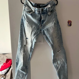 Ljusblå slitna skinny jeans - Säljer ett par ljusblå skinny jeans med rejält slitna detaljer och hål på både fram- och baksida. Jeansen har klassisk femficksdesign, dragkedjegylf och är tillverkade i bomull med stretch. Perfekta för dig som gillar en edgy och avslappnad stil.