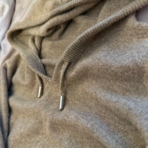 Kashmir hoodie  -  beige kashmir hoodie med huva och snörning med silvriga detaljer. Tröjan har lång ärm och ribbade muddar vid ärmslut och nederkant. Perfekt för dig som gillar en chill och enkel stil. Passar S men är lite i storleken