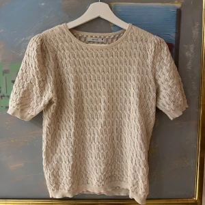 Beige stickad topp från Reserved - Säljer en beige stickad topp från Reserved med korta ärmar och rund hals. Tröjan har ett snyggt hålmönster och är gjord i ett mjukt material som känns luftigt!