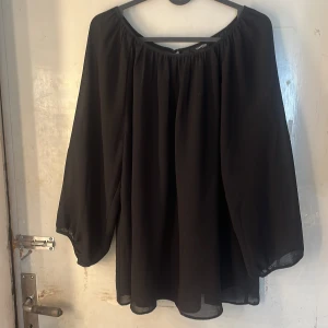 Svart blus  - Säljer en svart blus från Lindex  i storlek L. Blusen har vida, långa ärmar och en lös passform med rynkad, vid urringning. Tunt, lätt tyg som ger ett flowy intryck. Perfekt för dig som gillar en enkel men stilren look.